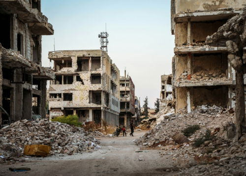 a man walking down a dirt road between two buildings